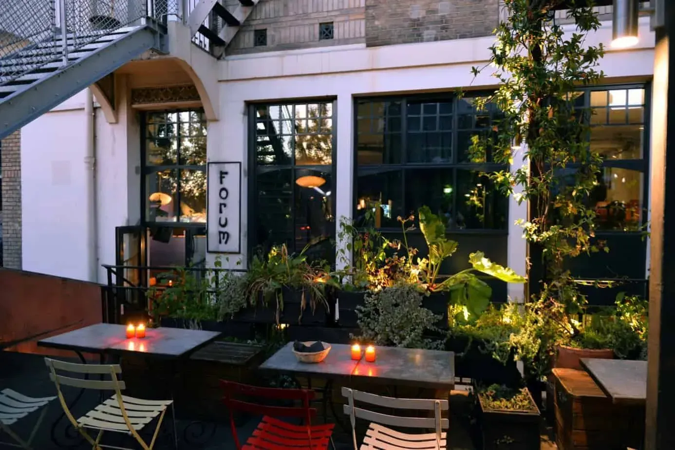 Terrace with potted plants, small tables and red and green chairs