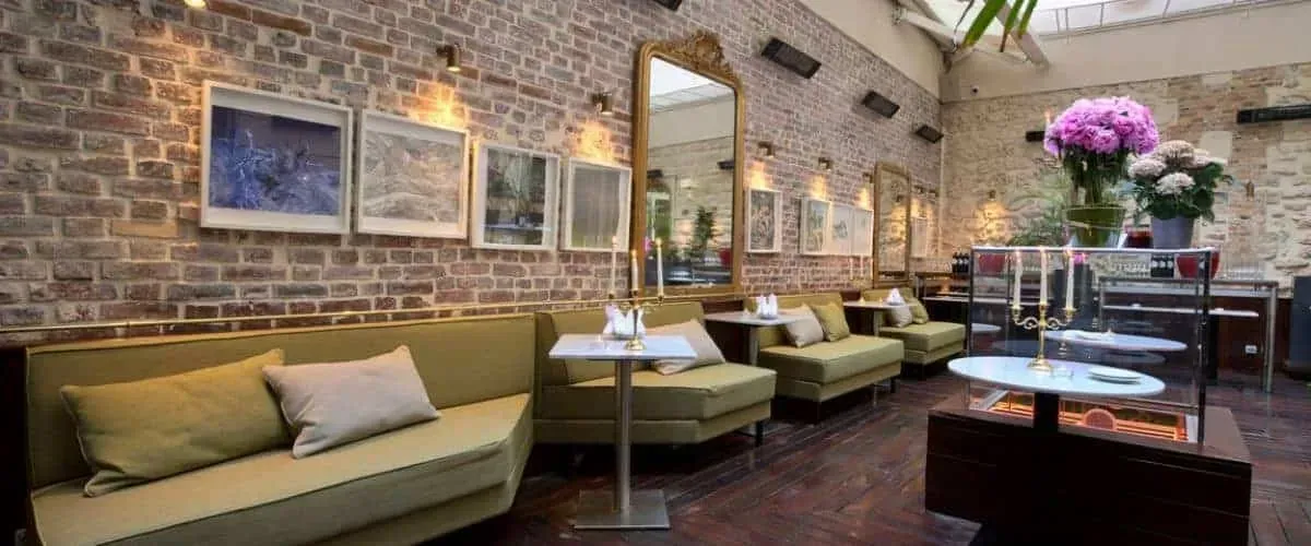 Brick-walled covered lounge with green sofas, mirrors and flowers