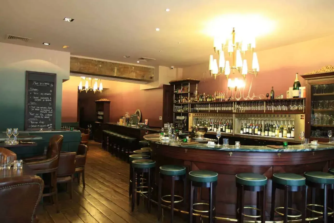 Bar with a long curved counter, green leather stools and hanging chandeliers